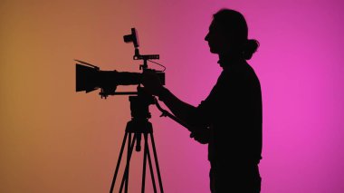 Bir siluet görüntüsü, bir kişiyi renkli bir arkaplan üzerinde kamera kullanırken gösteriyor..