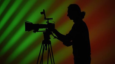 Stüdyo ortamında canlı ve renkli bir arkaplana karşı kamera kullanan bir kameramanın silüeti..