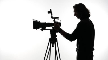 Video üretimini ve yaratıcılığını ön plana çıkaran, üç ayaklı bir kamerayı ayarlayan bir kişinin silüeti..