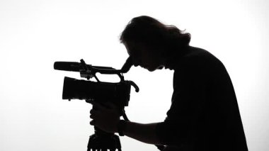 Profesyonel bir video kamerayla çekim yapan bir kişinin silueti, uzmanlık alanı ile büyüleyici görüntüler yakalıyor..