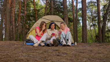 Bir grup arkadaş ormanda kamp yaparken eğlenceli bir anı paylaşıyorlar, çadırın dışında oturmuş doğanın tadını çıkarıyorlar. Yavaş çekim