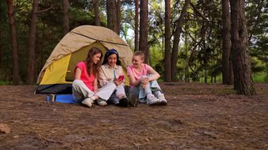 Bir grup arkadaş ormanda kamp yaparken eğlenceli bir anı paylaşıyor. Çadırın dışında oturmuş, doğanın tadını çıkarıyorlar..