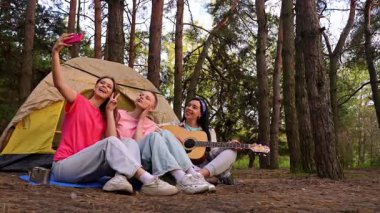 Üç arkadaş ormanda kamp yapmaktan zevk alıyor. Çadırlarının dışında selfie çekiyorlar ve gitar çalıyorlar..