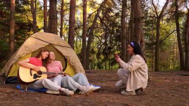 Arkadaşlarla dolu canlı bir kamp sahnesi müzik ve kahkahaların tadını çıkaran yemyeşil bir ormanda doğa ile çevrili..