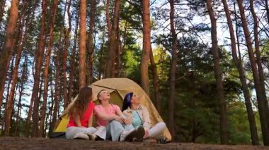 Yoğun bir ormanda çadırda kamp maceralarının keyfini çıkarırken üç kadın gökyüzünü neşeyle işaret ediyor..