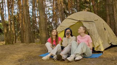 Üç arkadaş ormanda bir çadırda oturup, bir kamp gezisi sırasında içkinin ve arkadaşlığın tadını çıkarıyorlar..