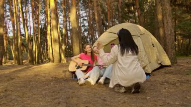 Arkadaşlarla dolu canlı bir kamp sahnesi müzik ve kahkahaların tadını çıkaran yemyeşil bir ormanda doğa ile çevrili..