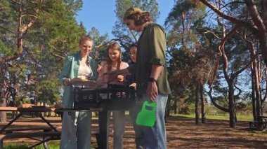 Bir grup arkadaş güneşli bir günün tadını çıkarıyorlar. Uzun ağaçlarla çevrili, pitoresk bir parkta barbekü yapıyorlar. Yavaş çekim