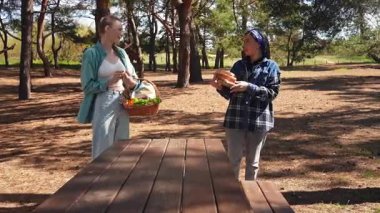Güneşli bir park ortamında piknik masasında dinlenen iki arkadaş, birbirine eşlik eden ve dışarıda eğlenen iki arkadaş..