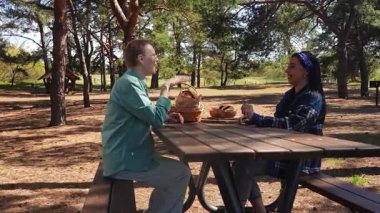 Güneşli bir park ortamında piknik masasında dinlenen iki arkadaş, birbirine eşlik eden ve dışarıda eğlenen iki arkadaş..