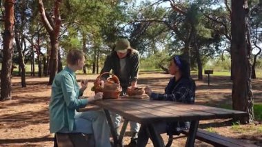 Güneşli bir park ortamında piknik masasında dinlenen üç arkadaş. Birbirine eşlik eden ve dışarıda eğlenen üç arkadaş..