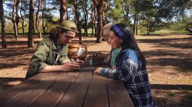 Bir grup arkadaş güneşli bir park ortamında piknik masasında dinleniyorlar, birbirlerine eşlik ediyorlar ve dışarıda eğleniyorlar..