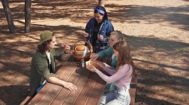 Bir grup arkadaş güneşli bir ormanda piknik yapıyorlar, sohbet ediyorlar ve açık havada taze sebzelerin tadını çıkarıyorlar..