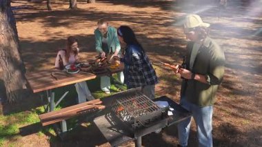 Bir grup arkadaş güneşli bir günün tadını çıkarıyorlar. Uzun ağaçlarla çevrili, pitoresk bir parkta barbekü yapıyorlar..