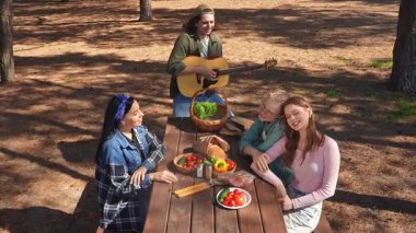 Bir grup arkadaş piknik için toplanır, güneşli bir açık hava ortamında yemek ve müziğin tadını çıkarırlar, rahatlamayı teşvik ederler..
