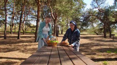 Güneşli bir park ortamında piknik masasında dinlenen iki arkadaş, birbirine eşlik eden ve dışarıda eğlenen iki arkadaş..