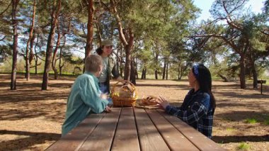 Güneşli bir park ortamında piknik masasında dinlenen üç arkadaş. Birbirine eşlik eden ve dışarıda eğlenen üç arkadaş..