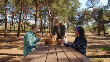Güneşli bir park ortamında piknik masasında dinlenen üç arkadaş. Birbirine eşlik eden ve dışarıda eğlenen üç arkadaş..