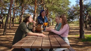 Bir grup arkadaş güneşli bir ormanda piknik yapıyorlar, sohbet ediyorlar ve açık havada taze sebzelerin tadını çıkarıyorlar..
