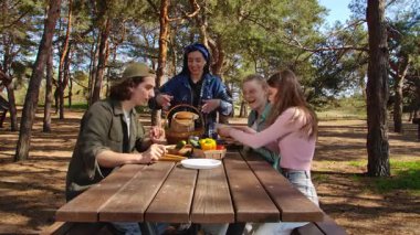 Bir grup arkadaş güneşli bir ormanda piknik yapıyorlar, sohbet ediyorlar ve açık havada taze sebzelerin tadını çıkarıyorlar..