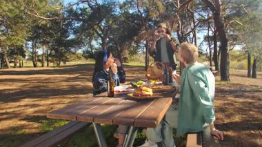 Bir grup park ortamında pikniğin tadını çıkarıyor. Dostça bir atmosferde ızgara sosis ve taze yiyecek paylaşıyorlar..