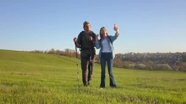 Geniş yeşil bir alanda yürüyüş yapan genç çift gün batımında yürüyüş direkleri ve sırt çantalarıyla doğanın tadını çıkarıyor. Telefonlarındaki bir video görüşmesinde sohbet ediyorlar.