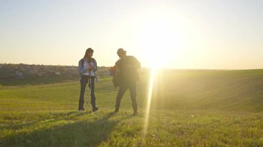İki yürüyüşçü çimenli bir arazide durur, güneşli havanın ve uzaktaki manzaranın tadını çıkarırlar..