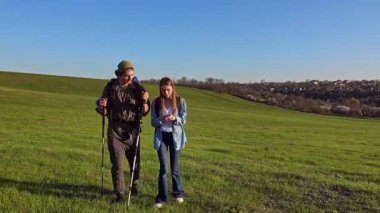 İki yürüyüşçü çimenli bir arazide durur, güneşli havanın ve uzaktaki manzaranın tadını çıkarırlar..