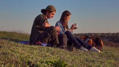 İki genç insan sessiz bir çimenlikte oturur, konuşur, ılık bir içki içer ve doğanın sakin atmosferinin tadını çıkarırlar..