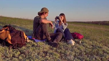 Genç bir çift çimenli bir tepede oturur kamerayla anları yakalar, doğanın güzelliğinin tadını çıkarırlar..