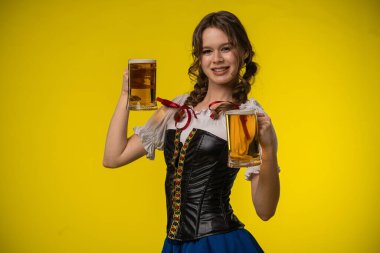 Geleneksel kostümlü gülümseyen genç bir kadın parlak sarı arka planda iki bira bardağı tutuyor..