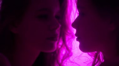 Yumuşak mor bir ışıkla aydınlatılmış aynaya bakan bir kadının yansımasını tasvir eden samimi bir sahne. Yavaş çekim