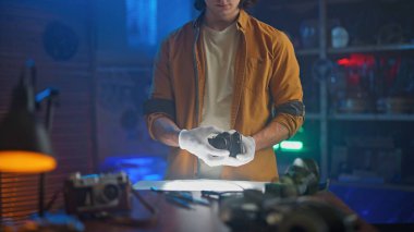 Eldiven giyen bir adam iyi aydınlatılmış bir masada eski bir kamerayı dikkatle inceler, hassasiyeti ve odaklanmayı vurgular..