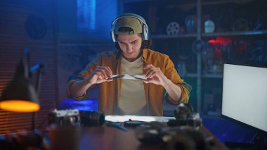 Kulaklıklı odaklanmış genç bir adam, karanlık bir odada, fotoğraf aletleriyle çevrili, negatif bir filmi inceliyor..