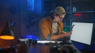 Genç bir adam donanımlarla çevrili loş, klasik bir fotoğraf laboratuvarında film işliyor..