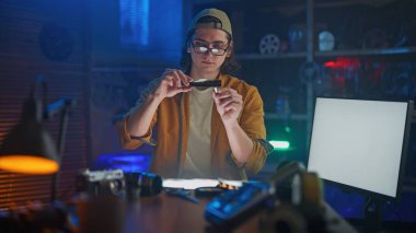 Yaratıcı bir stüdyoda genç bir adam, klasik fotoğraf ekipmanlarıyla çevrili yumuşak ışıklandırma altında negatif bir filmi yakından inceliyor..