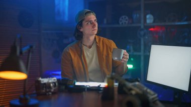 Genç bir adam, etrafındaki teknoloji ve aletlerle yaratıcı bir şekilde tasarlanmış çalışma alanında kahve molası veriyor..