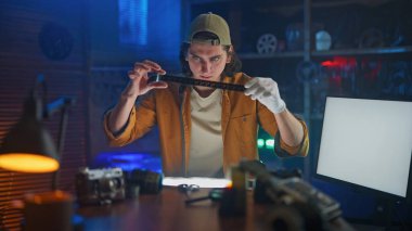 Odaklanmış genç bir fotoğrafçı, loş bir stüdyo ortamında gelişmiş bir film negatifini inceliyor..