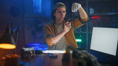 Genç bir adam, parlak ışık altında, loş bir odada, kesin profesyonel teknikler kullanarak, bir filmi dikkatle inceliyor..