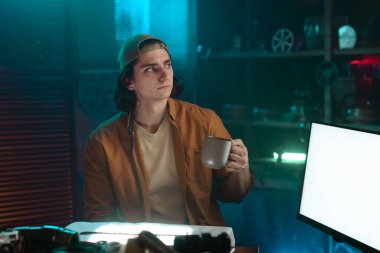 Bir insan loş bir odada şapka takar ve bardağı tutar. Ortam ışığı rahat bir atmosfer yaratıyor..