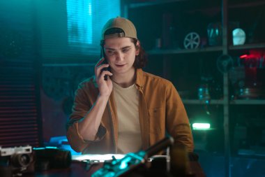 Atölye ortamında çalışan genç bir adam, yaratıcı aletlerle çevrili bir telefon görüşmesiyle meşgul..