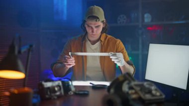 Şapkalı ve eldivenli genç bir adam stüdyo ortamında bir kamera filmini inceliyor, analog fotoğrafçılığa ilgi gösteriyor..