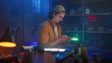 Sarı tişörtlü ve şapkalı genç bir adam şık ve modern bir atölye ortamında akıllı telefonunu kullanıyor..