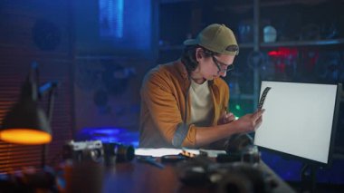 Yaratıcı bir stüdyoda genç bir adam, klasik fotoğraf ekipmanlarıyla çevrili yumuşak ışıklandırma altında negatif bir filmi yakından inceliyor..