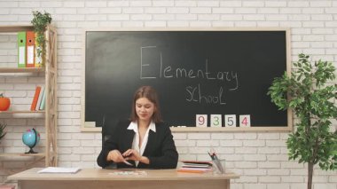 Okul öğretmeni sınıfta öğrencilere konuşuyor. Karatahtanın önündeki masada oturan genç bayan üniversite öğretmeni ilkokul çocuklarına astronomi dersi veriyor. Eğitim kavramı.