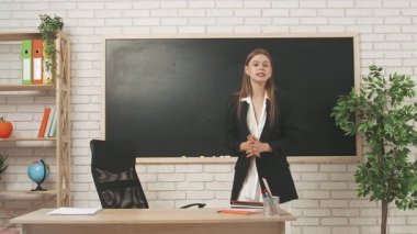 Okul öğretmeni sınıfta öğrencilere konuşuyor. Genç bayan üniversite öğretmeni sınıfın önünde durmuş tahtayla konuşuyor ve öğrencilere materyalleri anlatıyor. Eğitim kavramı.