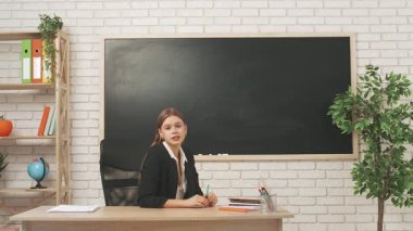 Okul öğretmeni sınıfta öğrencilere konuşuyor. Sınıftaki masada oturan genç bayan üniversite öğretmeni öğrencilere geometri dersini açıklıyor, çizimler çiziyor. Eğitim kavramı.