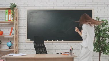 Okul öğretmeni sınıfta çalışır. Genç bayan kolej öğretmeni dans ederek ve şarkı söyleyerek odaya girer, sınıfın masasında tahtaya oturur. Eğitim kavramı.
