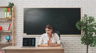 Okul öğretmeni sınıfta öğrencilere konuşuyor. Sınıftaki masa başında oturan kadın üniversite öğretmeni öğrencilere biyoloji dersini açıklıyor, dizüstü bilgisayarında video materyali gösteriyor. Eğitim kavramı.