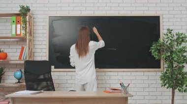 Okul öğretmeni sınıfta öğrencilere konuşuyor. Sınıftaki masada oturan genç bayan üniversite öğretmeni, tahtaya yazı yazarak öğrencilere geometri dersi veriyor. Eğitim kavramı